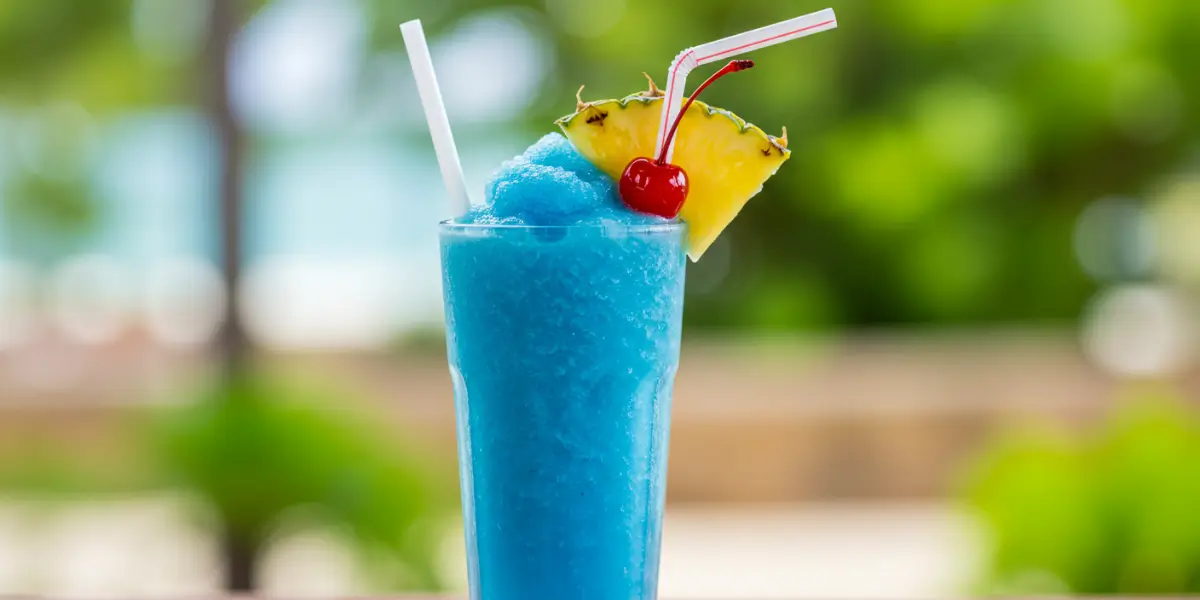 A tall glass filled with a vibrant, frosty blue Piña Colada smoothie, garnished with a pineapple wedge.
