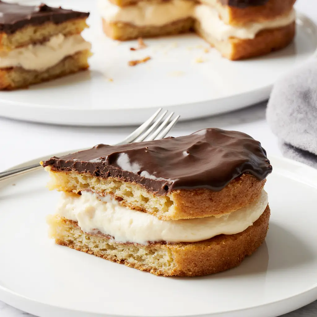 Slice of chocolate éclair cake displaying three layers: golden choux pastry base, creamy vanilla custard filling, and glossy dark chocolate ganache topping on a white plate
