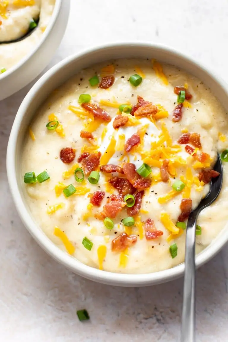 Creamy baked potato soup garnished with crispy bacon, melted cheddar cheese, fresh chives, and sour cream in a white bowl