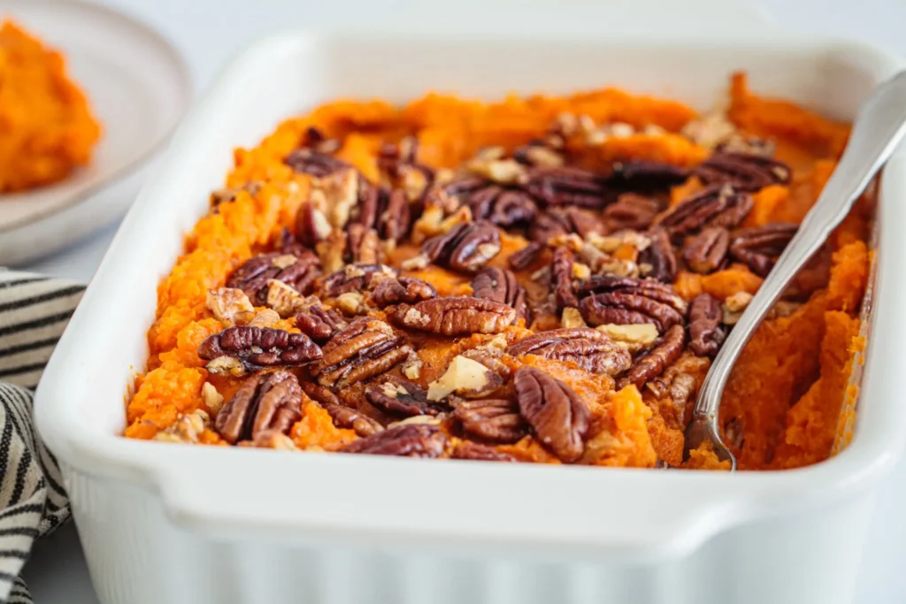 Close-up of a serving of sweet potato casserole with a crunchy pecan streusel topping and fresh pecans scattered on the plate.